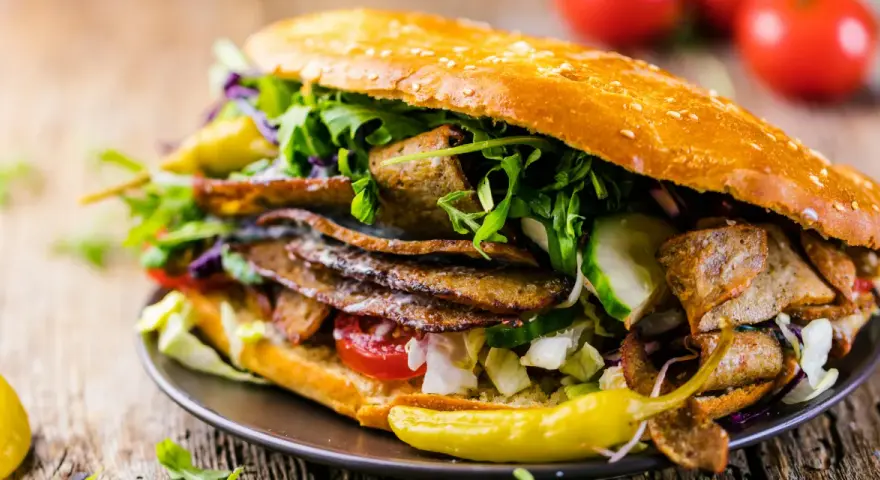 Duży kebab w bułce z mięsem, warzywami i sosem na drewnianym tle.