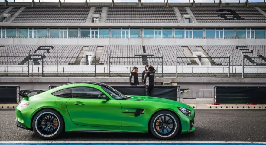 Zielony Mercedes GTR na torze wyścigowym, gotowy do jazdy. Za nim puste trybuny stadionu.
