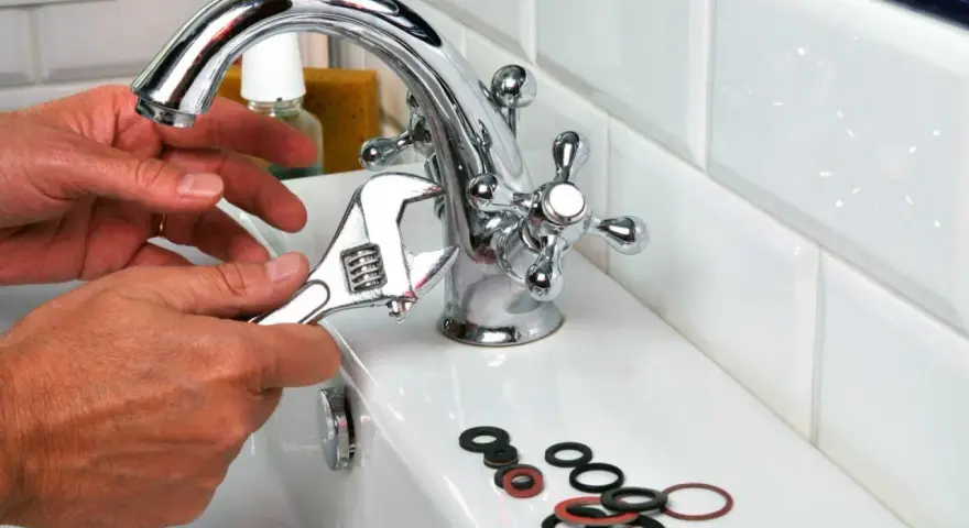 Main tenant utilise une clé pour changer un joint de robinet. Des joints sont posés sur le lavabo.