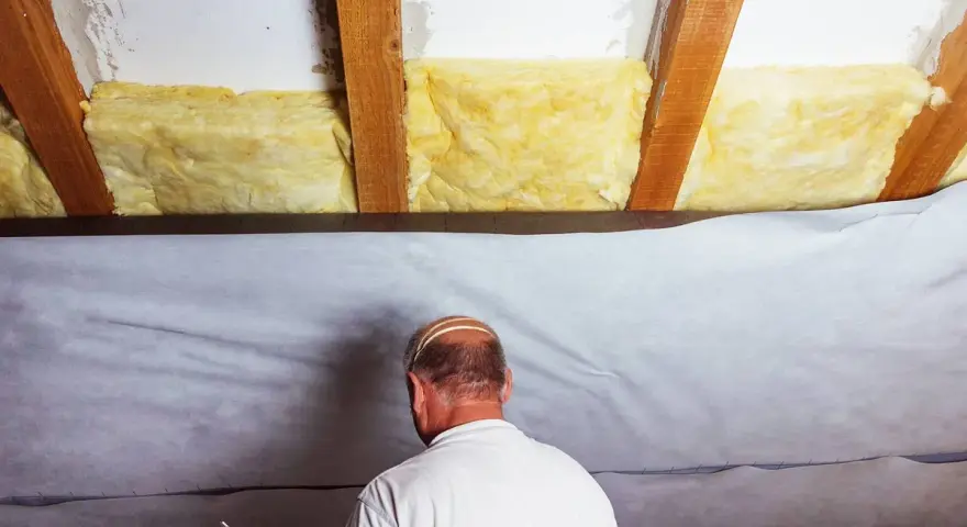 Mann dichtet das Dach von innen ab, indem er Dämmmaterial und eine Folie anbringt.
