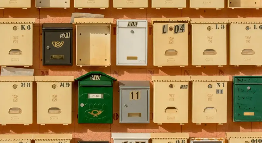 Rangées de boîtes aux lettres de copropriété, certaines jaunes, une verte, une noire et une blanche, avec des numéros et des symboles.