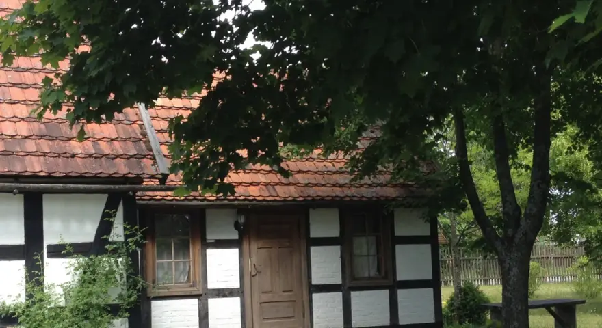 Urokliwa chata kaszubska z drewnianymi belkami i czerwoną dachówką, otoczona zielenią.