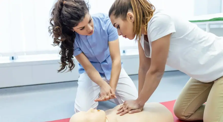 Zwei Frauen üben kardiopulmonale Reanimation an einer Übungspuppe. Eine Frau gibt Anweisungen, während die andere die Herzdruckmassage durchführt.
