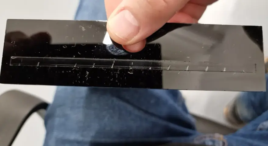 A hand holds a black acrylic strip with a precisely cut slot, demonstrating how to laser cut acrylic at home.