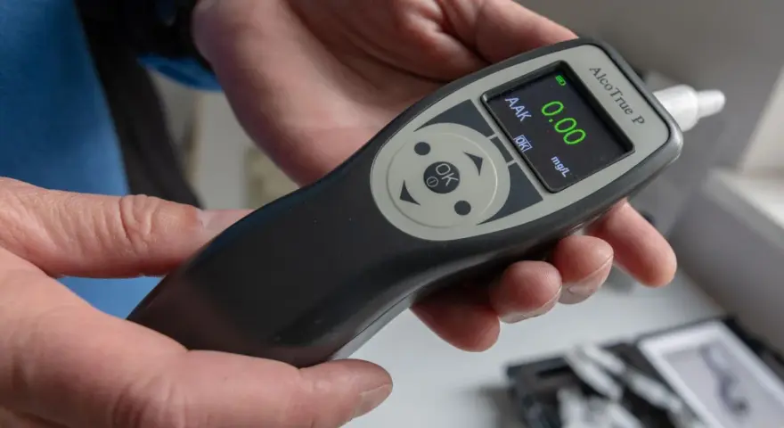Hände halten ein Alkoholtestgerät, das 0.00 mg/L anzeigt. So vermeidet man eine Strafe wegen Alkohol am Steuer.