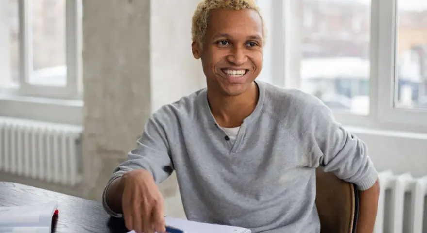 Lächelnder Mann mit blonden Haaren sitzt am Schreibtisch, Notizbuch und Stift bereit für sein Praktikum in Deutschland.