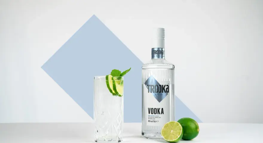 Ein Glas mit Eis, Limette und Minze steht neben einer Flasche Trojka Wodka. Perfekt für einen erfrischenden Wodka mit Wasser.