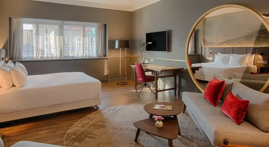 Modern hotel room with a bed, sofa, desk, and large round mirror reflecting the room.