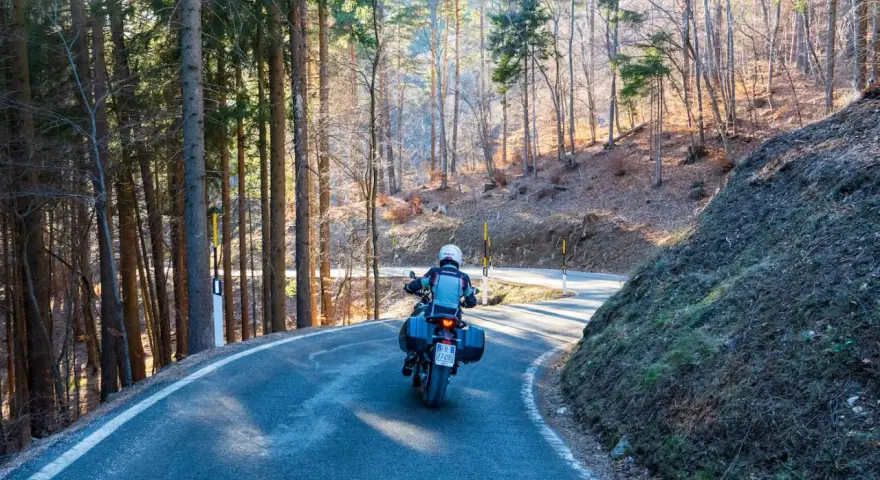 Motociclista su strada tortuosa tra i boschi, un'avventura **rund um den Gardasee**.
