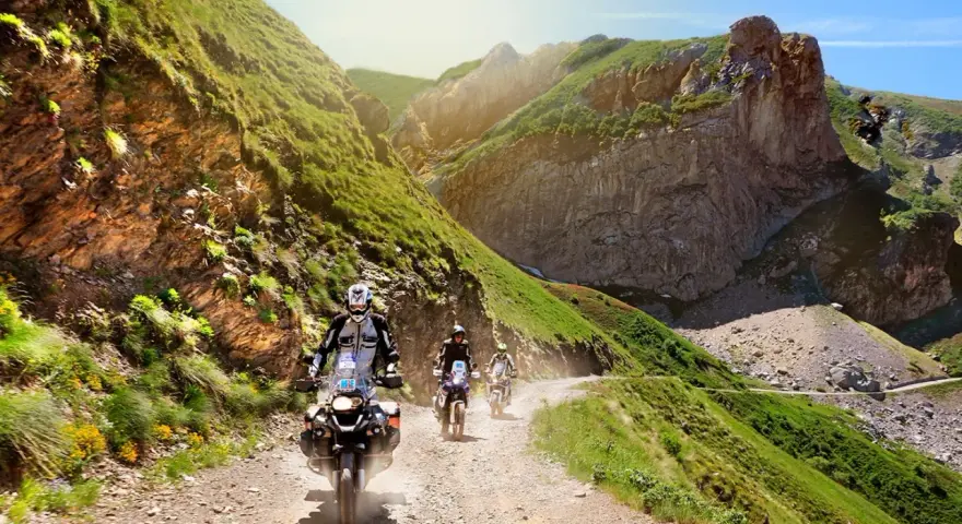 Un gruppo di motociclisti affronta un emozionante giro in moto in Liguria, su una strada sterrata tra montagne verdi e rocce imponenti.
