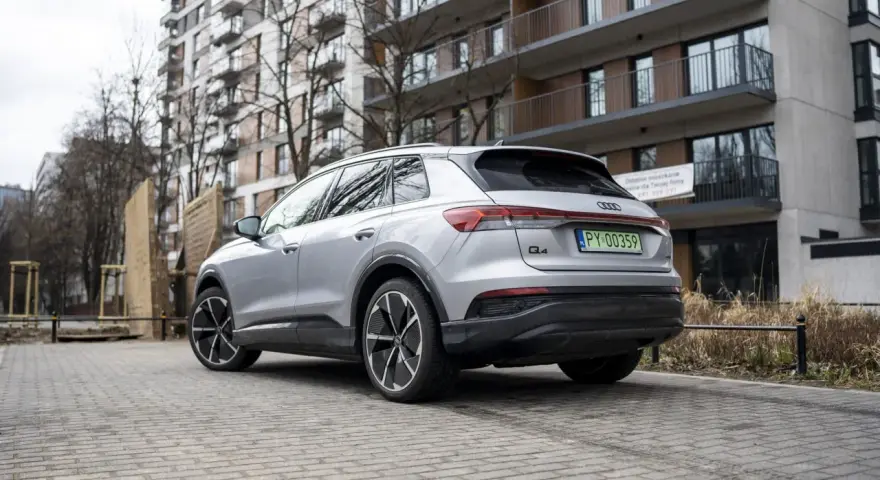 Srebrny Audi Q4 e-tron zaparkowany przed nowoczesnym budynkiem mieszkalnym.