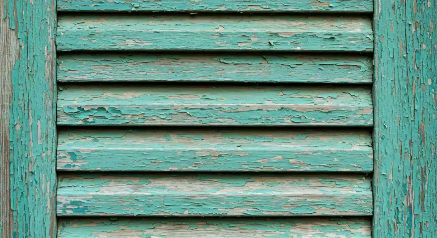 Persiane in legno fai da te con vernice verde acqua scrostata, che rivela il legno grezzo sottostante.