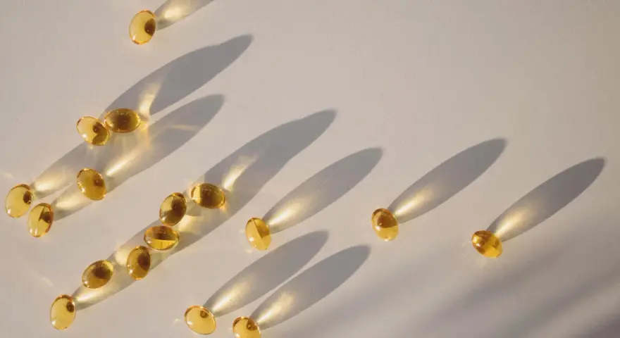 Gula kapslar med d-vitamin och magnesium sprids ut på en ljus yta, med långa skuggor som skapas av solljuset.