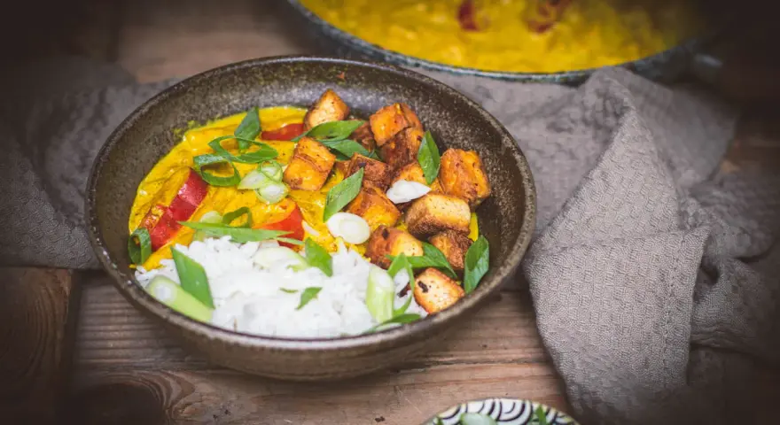 Aksamitne mango curry z ryżem, chrupiącym tofu i świeżą bazylią. Danie prezentuje się apetycznie.