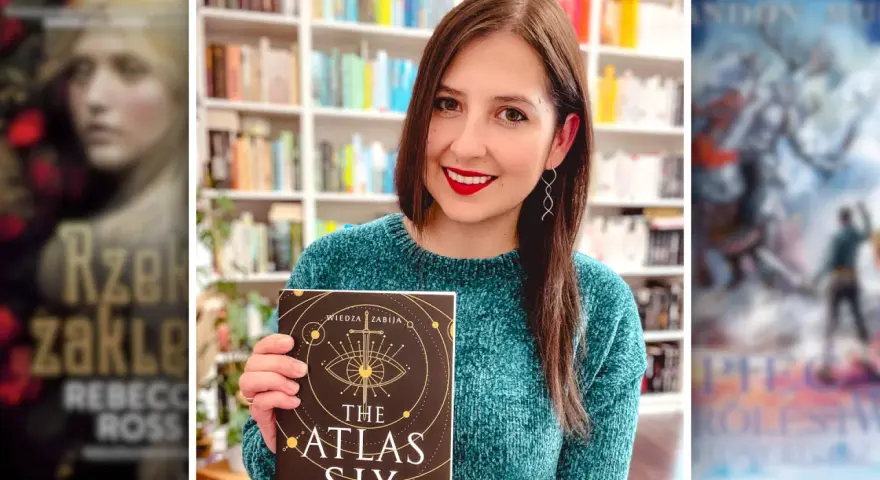 Uśmiechnięta kobieta trzyma książkę "The Atlas Six". W tle widać półki z książkami, w tym inne serie książek fantasy.
