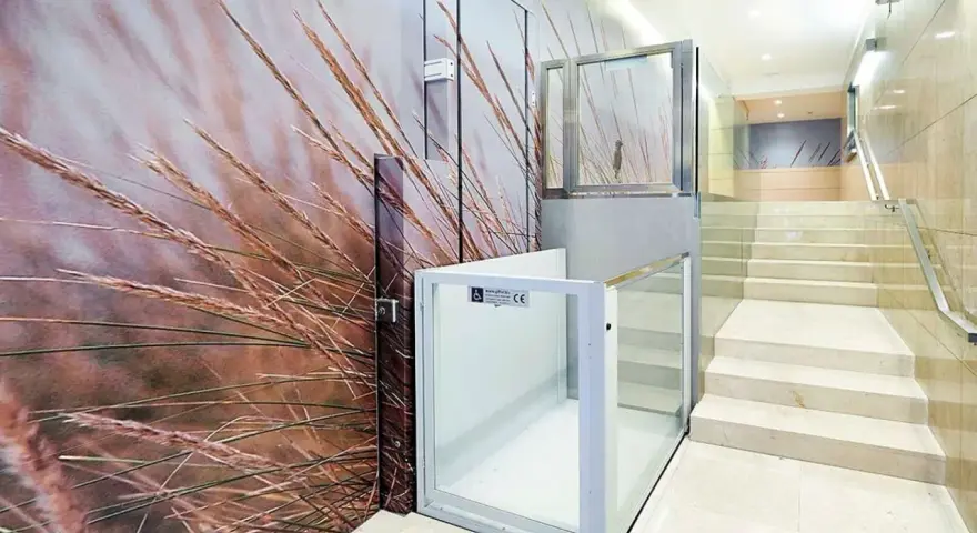 Un portal de vecinos moderno con un mural de hierbas secas y una plataforma elevadora de cristal.