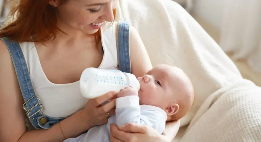 Uśmiechnięta mama karmi piersią swoje dziecko z butelki, szukając najlepszych butelek dla noworodka.