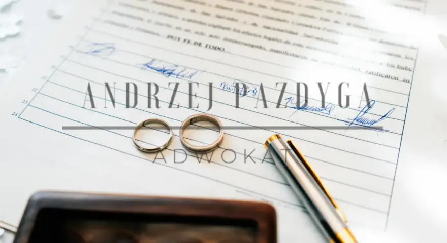 Dwa obrączki na dokumencie z podpisami i nazwiskiem "Andrzej Pazdyga", sugerujące intercyzę po ślubie. Obok pióro i drewniane pudełko.