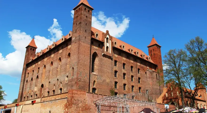 Potężny zamek w Gniewie, ceglana twierdza z wieżami i czerwonymi dachami, pod błękitnym niebem. Ciekawostki o jego historii czekają na odkrycie.
