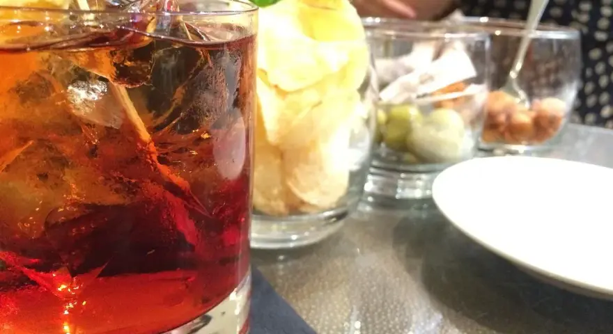 Orzeźwiający drink z lodem i cytryną, obok chipsy i oliwki. Idealne połączenie, by dowiedzieć się, **sambuca z czym pić**.