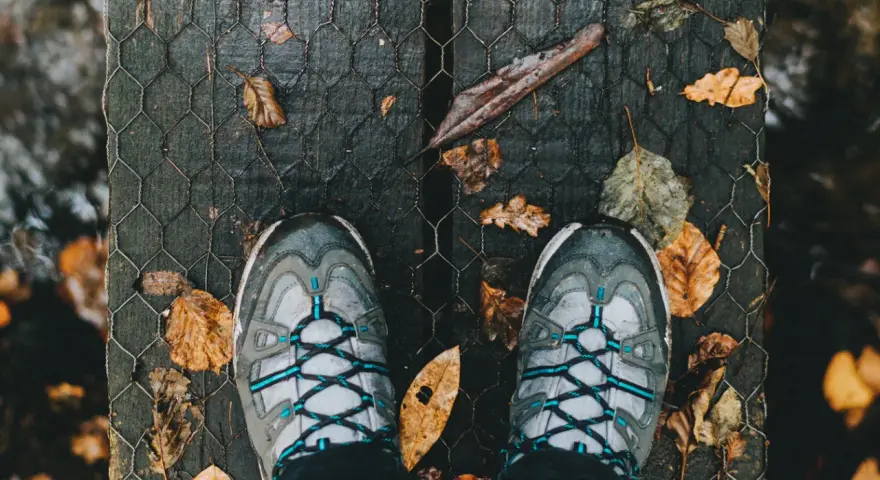 Scarpe in Gore-Tex donna pronte per un'avventura autunnale su un ponte di legno coperto di foglie.