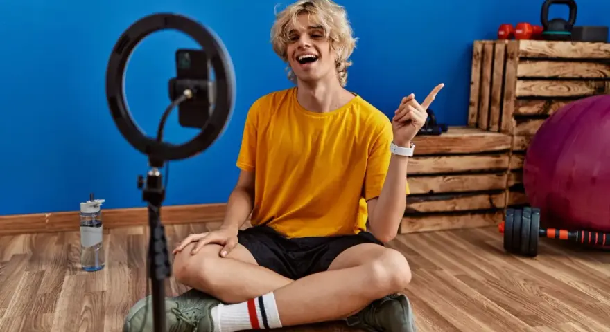 Joven influencer de fitness sonríe y señala, listo para grabar sus acciones con influencers.