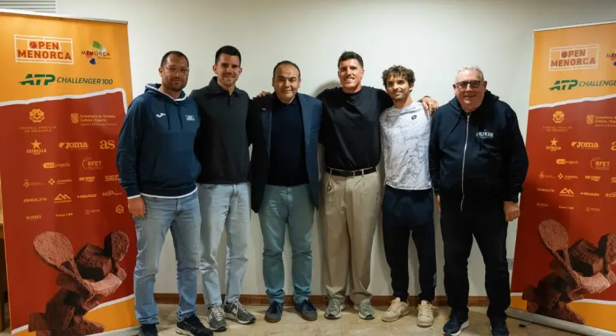 Roberto Carballes Baena posa con otros hombres frente a un cartel del Open Menorca ATP Challenger 100.
