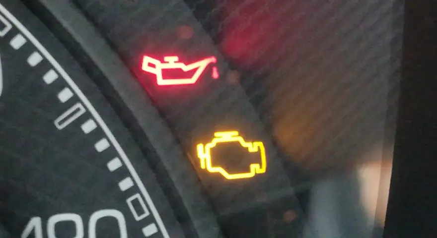 Cruscotto auto con spia dell'olio accesa in rosso e spia motore gialla. Urgente controllo.