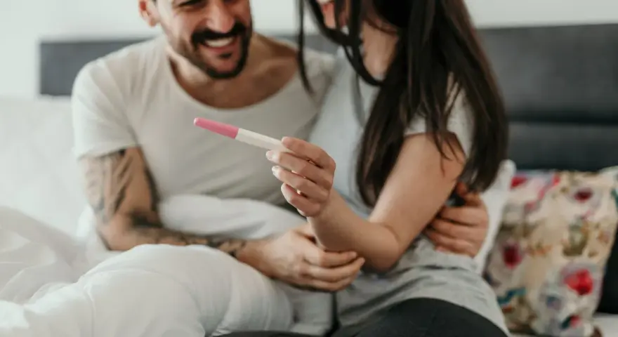 Ein Paar hält einen Schwangerschaftstest, der positiv ist. Was zeigt ein Ovulationstest an, wenn man schwanger ist? Zwei rosa Linien.