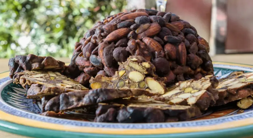 Un pan pepato a forma di cupola, ricoperto di mandorle e cacao, con fette tagliate che rivelano frutta secca e spezie.