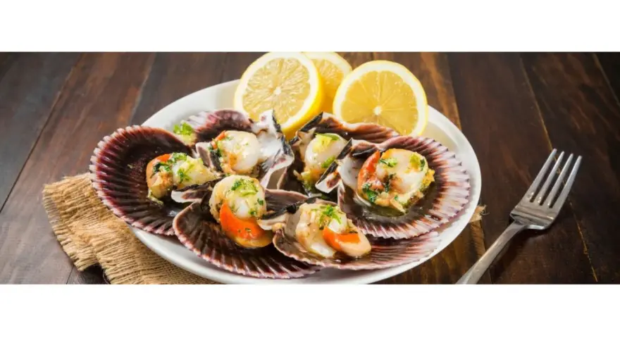 Zamburiñas a la plancha servidas en sus conchas, adornadas con perejil picado y rodajas de limón. Un plato delicioso y fresco.