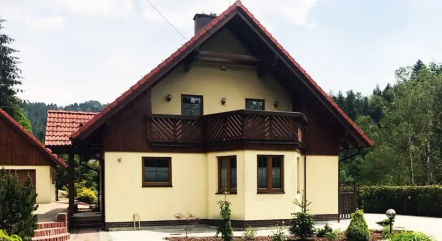 Jasny dom z drewnianymi elementami i balkonem, otoczony zielenią. Może to być dom Adama Małysza w Wiśle.