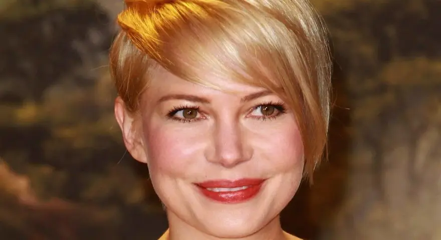 Uśmiechnięta kobieta z okrągłą twarzą i blond fryzurą, z burzą złotych włosów opadających na czoło.