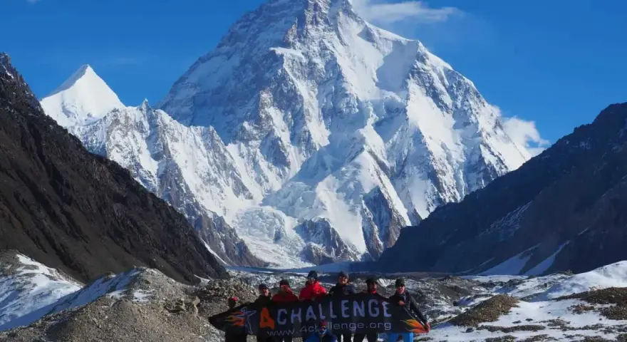 Grupa ludzi z banerem przed majestatycznym szczytem K2 w Karakorum. To wyzwanie w górach Pakistanu.