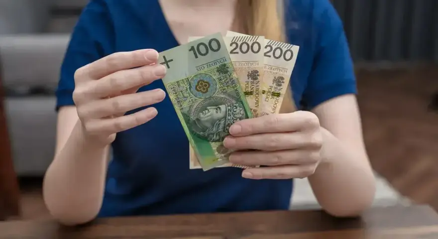 Dłonie trzymają polskie banknoty: 100 zł i dwa razy po 200 zł. To może być część zasiłku rodzicielskiego.