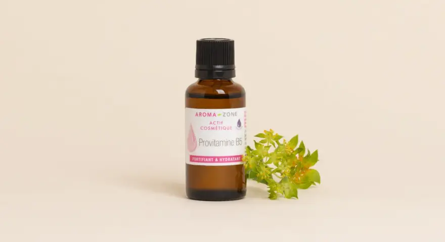 Flacone di Provitamina B5, un attivo cosmetico fortificante e idratante per la pelle, accanto a un rametto fiorito.