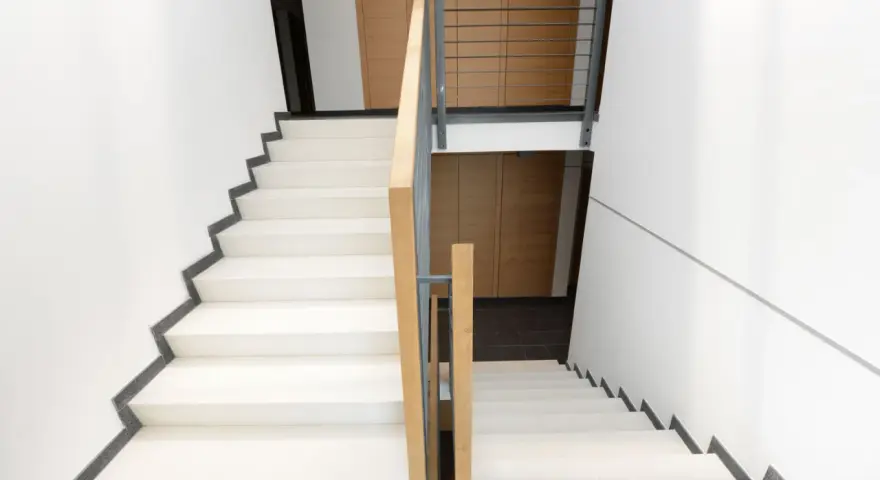 Nowoczesne schody z jasnymi stopniami i drewnianą balustradą. Każdy podstopnica jest wyraźnie zaznaczona.