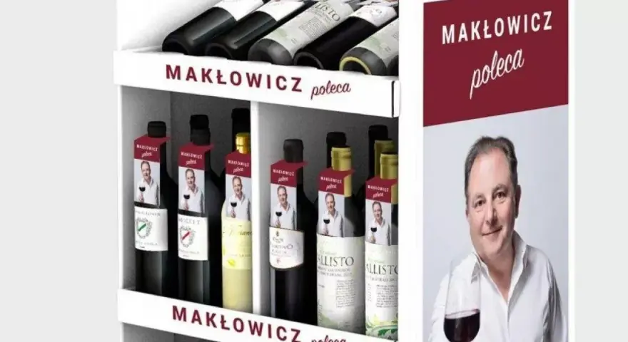 Regał z butelkami wina, z etykietami "Makłowicz poleca" i zdjęciem Roberta Makłowicza.
