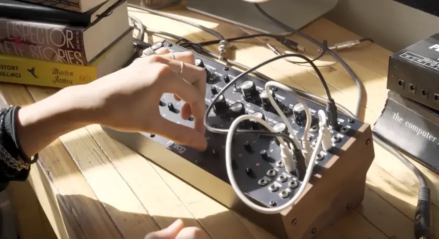 Ręka manipuluje pokrętłami na syntezatorze Moog DFAM, tworząc dźwięki.