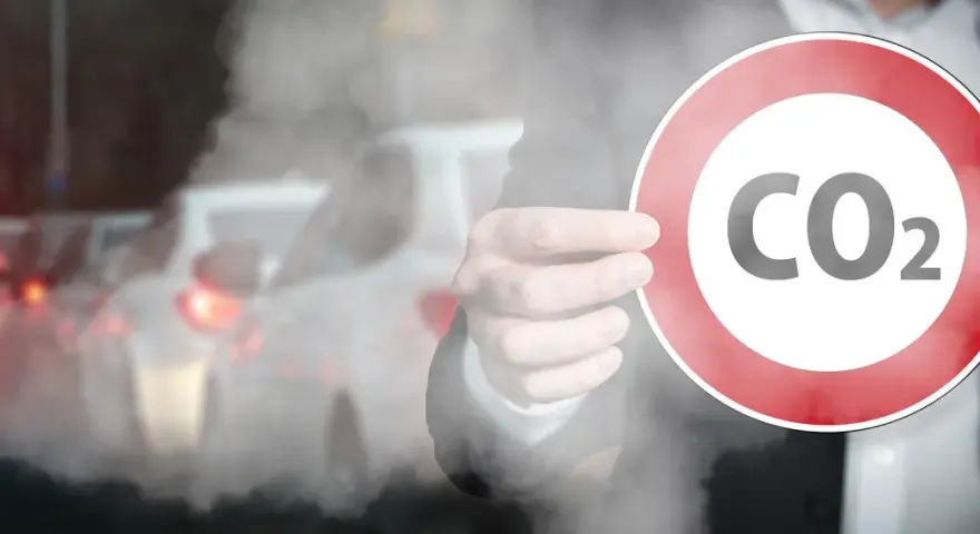 Dłoń trzyma znak zakazu z napisem CO2 na tle dymiących samochodów w korku.
