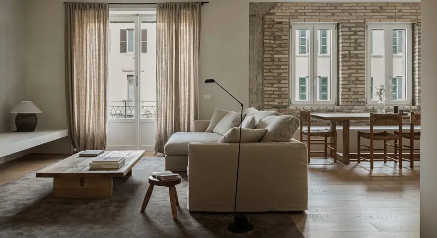 Un accogliente divano in mezzo alla stanza, con un tavolino in legno grezzo e un tappeto scuro.