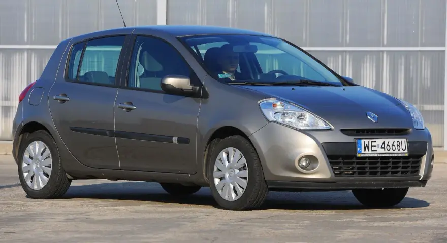 Szary Renault Clio 3 z kierowcą za kierownicą, zaparkowany na zewnątrz.