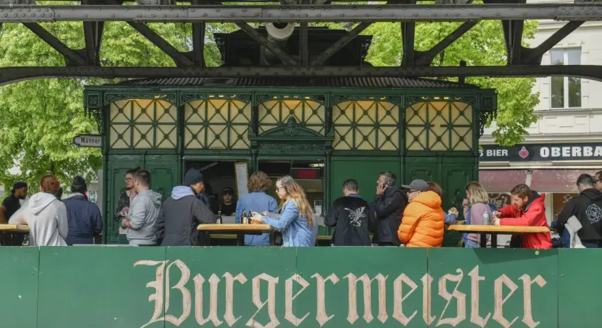 Menschen sitzen an Tischen vor dem Burgermeister in Berlin.