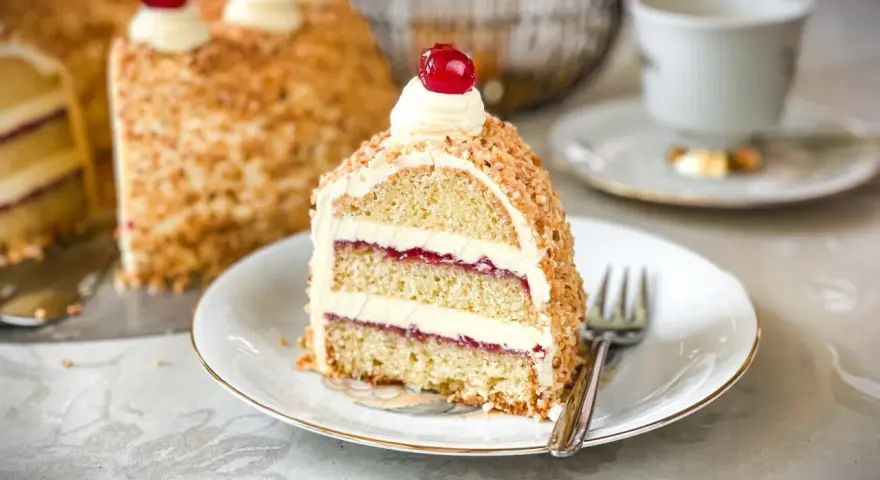 Ein Stück einer köstlichen Torte mit Buttercreme und roter Marmelade, umhüllt von gehackten Nüssen. Perfekt für die besten Torten Rezepte!