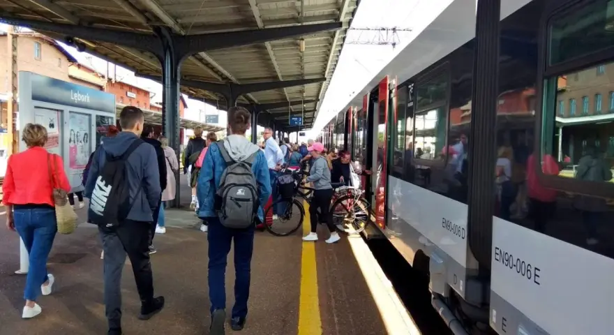 Ludzie czekają na pociąg na stacji w Lęborku. W tle widać budynek dworca i peron.