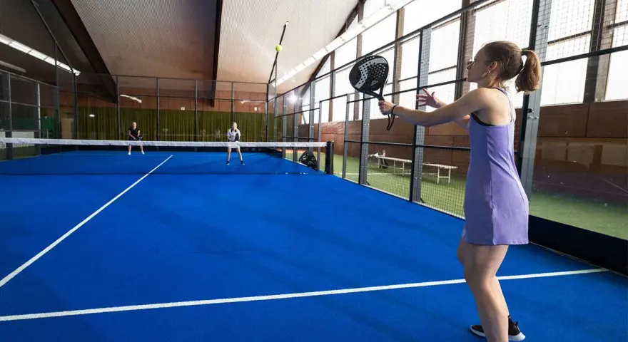 En kvinna i lila klänning spelar padel. Hon är redo att slå bollen på den blå banan.