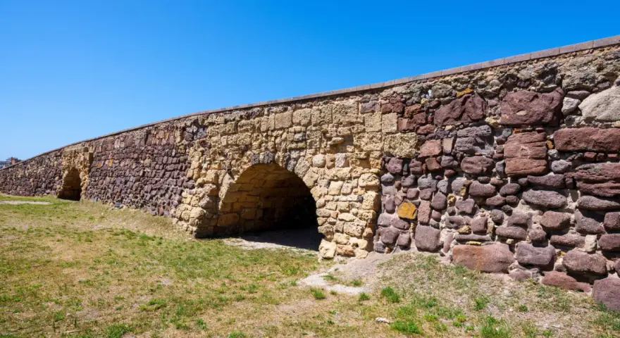 Antico ponte romano a Sant'Antioco, con archi in pietra e un muro imponente sotto un cielo azzurro.