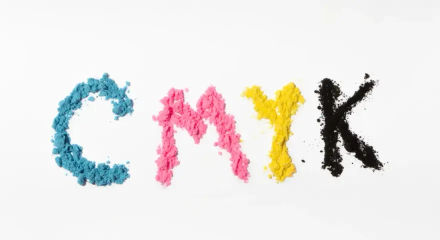 Litery CMYK ułożone z kolorowego proszku. Kolejność kolorów: cyjan, magenta, żółty, czarny.