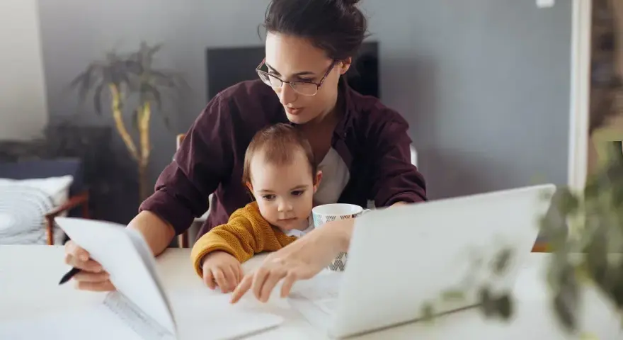 Mama z dzieckiem przy biurku, pracująca zdalnie. Kosiniakowe dla kogo? Dla rodziców łączących pracę z opieką nad dzieckiem.