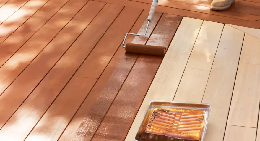 Aplicando protector para proteger madera exterior. Un rodillo extiende el líquido sobre las tablas de madera de una terraza.